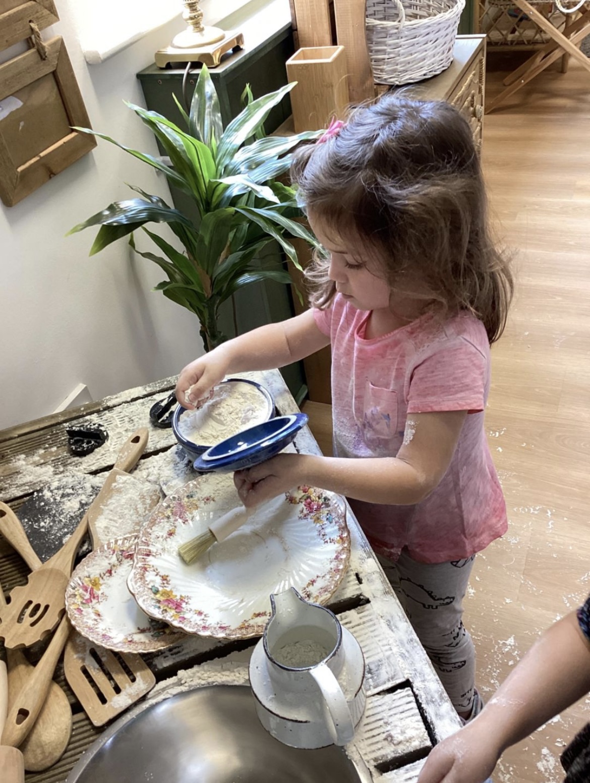 A young child exploring flour play with vintage plates, bowls and wooden utensils at Wibli Wobli Newport