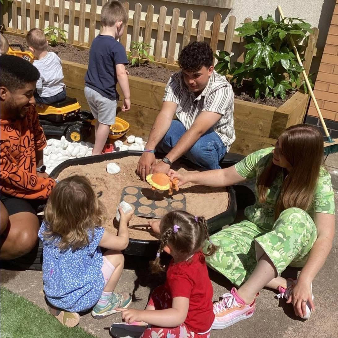 Children and practitioners playing together in a large outdoor sand tray at Wibli Wobli Newport