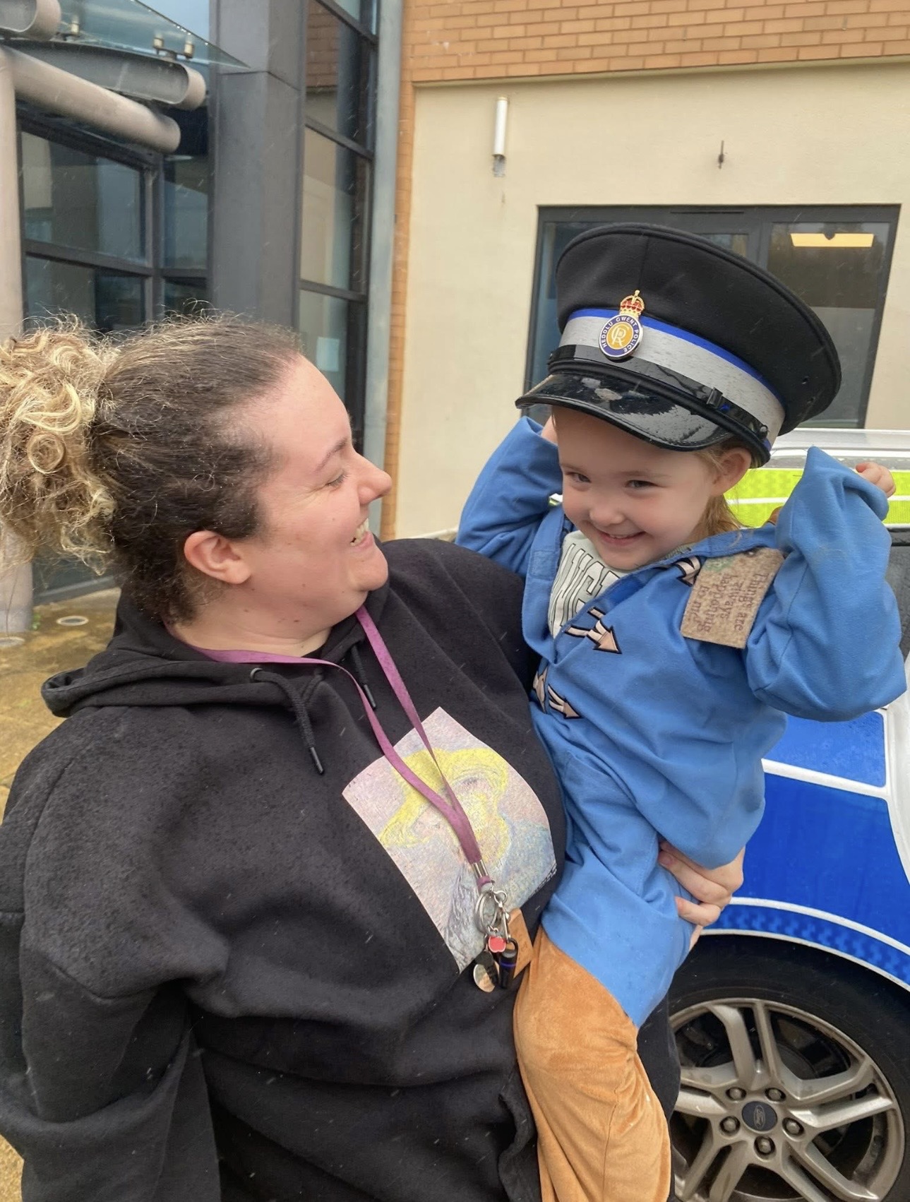 A Wibli Wobli practitioner holding a child who is trying on a police hat during a community visit